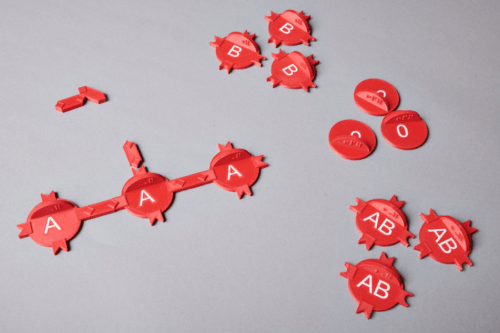 An example picture of a 3D print with two colors. This is a mechanic representation of different kinds of blood cells. The cells are colored in red, letters are designed on top of the blood cells in white (A,B, AB, 0), so you can immediately see which blood cells are which.