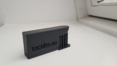 A black structure with an overhang in the state that it stands on the build plate when the print is done. Support is still attached to the structure.
